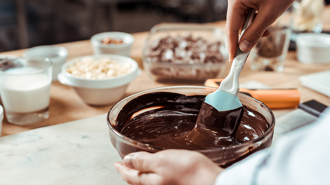 cukiernik miesza masę czekoladową w misce na stole ze składnikami